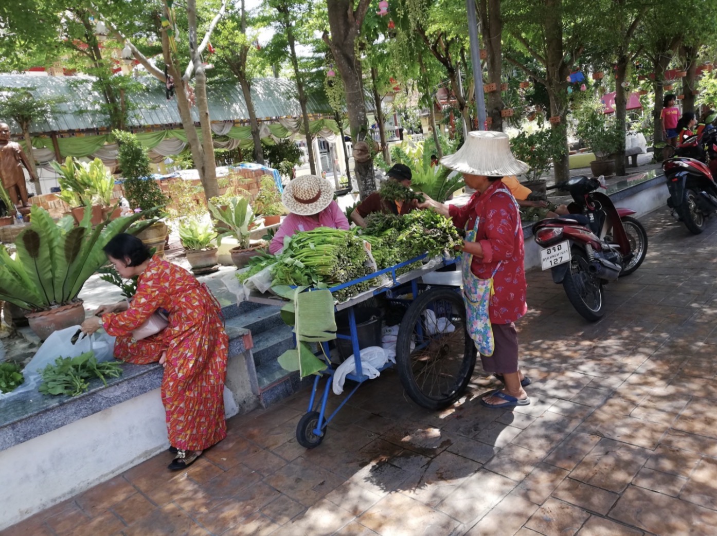 木陰で野菜を売る人々が行き交うタイの市場